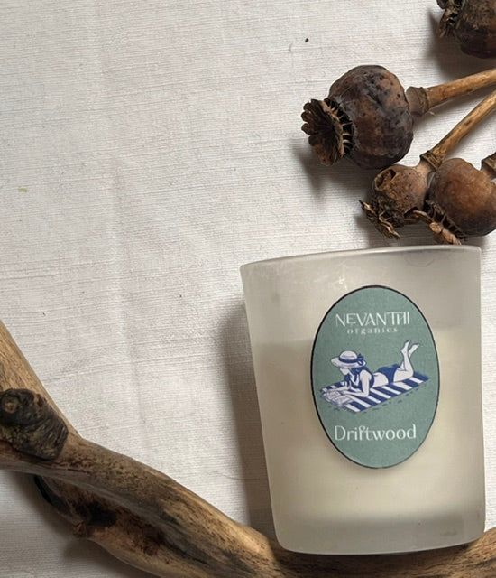 Driftwood takeaway candle by Nevanthi Organics — frosted glass mini soy wax candle with sage and sea salt styled with driftwood and dried poppy heads on white linen