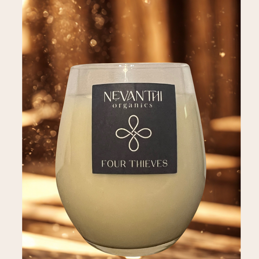 Glass candle with Nevanthi Organics Four Thieves label against a warm, blurred background